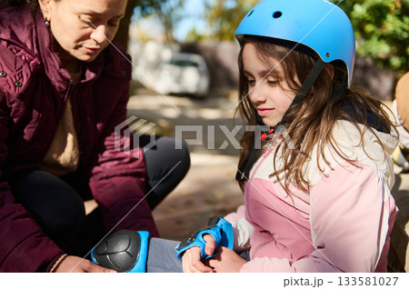 Young Girl in Blue Bike Helmet Receives Help Outdoors During Family Activity 133581027