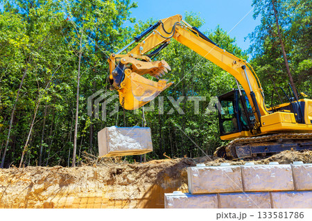 Heavy machinery moves large stone block at busy construction site with for retaining wall Heavy machinery moves large stone block at busy construction site with for retaining wall 133581786