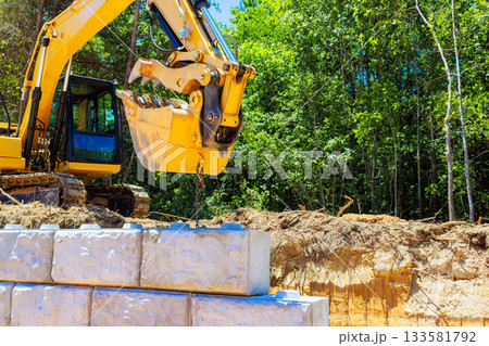 Heavy machinery lifts large blocks at construction site wooded under creating retaining wall Heavy machinery lifts large blocks at construction site wooded under creating retaining wall 133581792