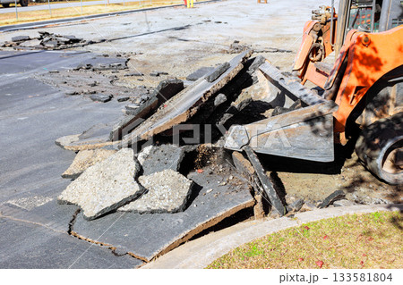 Construction skid steer is clearing debris from damaged pavement during road repair 133581804