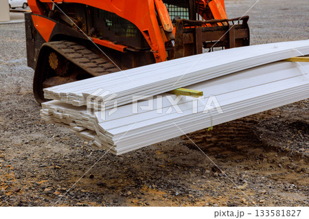 Heavy machinery transports long white wooden beams at busy construction site 133581827