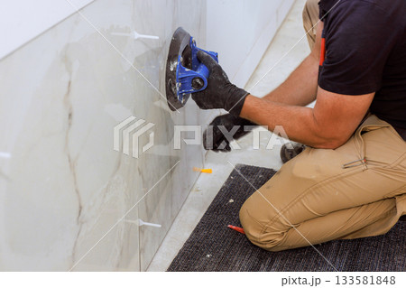 Skilled worker carefully applies tiles to wall, ensuring accuracy quality in contemporary setting. 133581848
