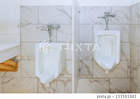 Two modern urinals are placed side by side in tiled restroom with bright lighting simple design. Two modern urinals are placed side by side in tiled restroom with bright lighting simple design. 133581881