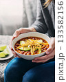 Cozy bowl of chili with avocado slices in hands 133582156