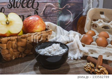 Rustic kitchen scene with fresh preparation of a gourmet dessert with red apples, cinnamon, eggs and nuts. Rustic kitchen scene with fresh preparation of a gourmet dessert with red apples, cinnamon, eggs and nuts. 133582789