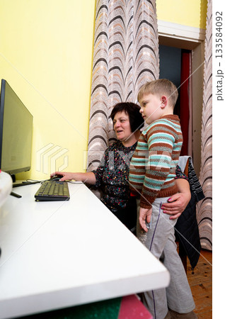 Grandmother shares an engaging moment with her grandson at home while exploring the wonders of technology in a cozy living room setting 133584092
