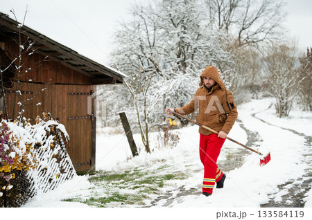 Snowy winter day brings a worker outside to clear the path near a rustic cabin surrounded by trees blanketed in white 133584119