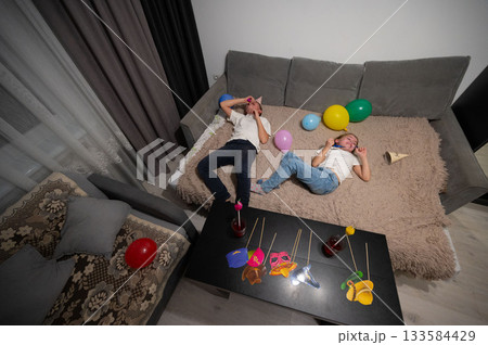 Joyful celebration with children lying on a cozy couch surrounded by colorful balloons and playful decorations in a festive indoor setting at night Joyful celebration with children lying on a cozy couch surrounded by colorful balloons and playful decorations in a festive indoor setting at night 133584429