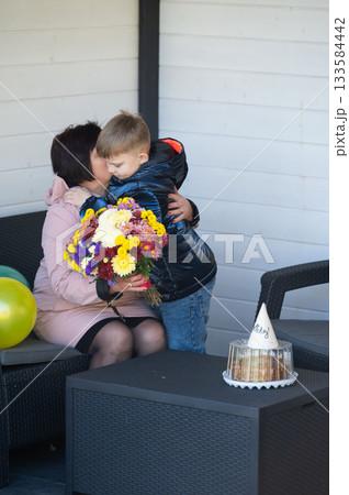 Emotional embrace between mother and son celebrating a special day with flowers and decorations in a cozy outdoor setting on a sunny afternoon Emotional embrace between mother and son celebrating a special day with flowers and decorations in a cozy outdoor setting on a sunny afternoon 133584442