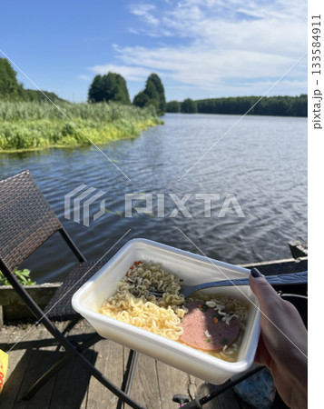 Instant noodles in plastic bowl by lake, outdoor camping lunch 133584911