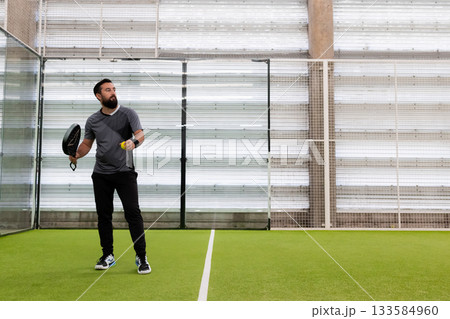 Young hispanic male playing padel tennis in indoor court 133584960