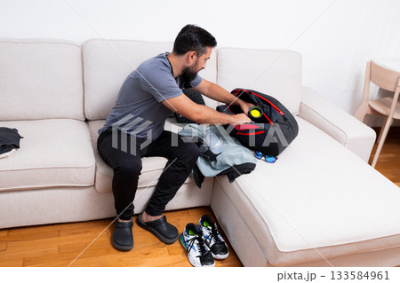 Young caucasian male packing gym bag on couch with fitness gear 133584961