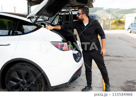 Male cleaning car trunk at charging station 133584966