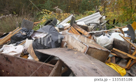 heap of mixed construction household debris on roadside with visible rust and loose insulation; plastic sacks, metal drums and broken panels suggest contamination risk and need for urgent 133585186