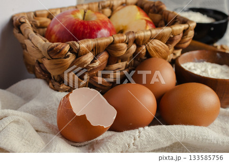 Bakery ingredients for homemade apple desserts with eggs, flour, and fresh fruit, preparing a rustic recipe with natural products on a textured linen cloth Bakery ingredients for homemade apple desserts with eggs, flour, and fresh fruit, preparing a rustic recipe with natural products on a textured linen cloth 133585756