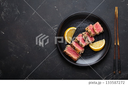 Seared grilled tuna steak tataki slices sesame seeds lemon black plate healthy delicacy space for text Seared grilled tuna steak tataki slices sesame seeds lemon black plate healthy delicacy space for text 133587272