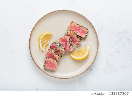 Seared grilled tuna steak tataki slices sesame seeds lemon white plate delicacy asian Japanese 133587307
