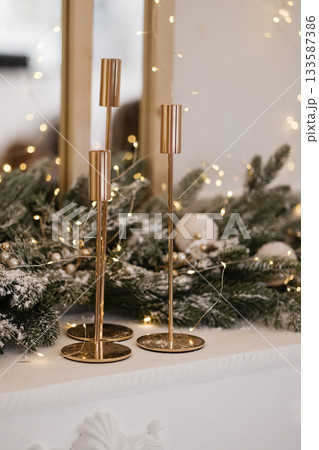 Gold candle holders on white mantel with Christmas greenery and warm lights Gold candle holders on white mantel with Christmas greenery and warm lights 133587386