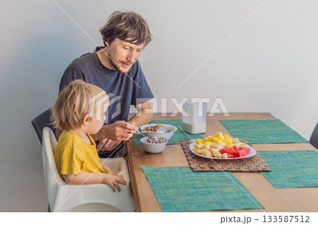 A father having breakfast at the table with his young son in a bright home kitchen, sharing a warm morning moment. Family bonding, parenting, everyday routine and healthy lifestyle concept A father having breakfast at the table with his young son in a bright home kitchen, sharing a warm morning moment. Family bonding, parenting, everyday routine and healthy lifestyle concept 133587512