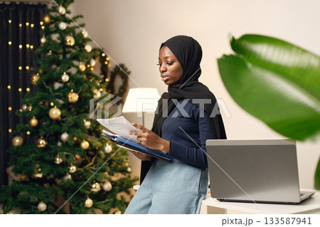 Young muslim business woman standing in her office. Woman holding documents. Woman wearing blue shirt and black hijab. Young muslim business woman standing in her office. Woman holding documents. Woman wearing blue shirt and black hijab. 133587941
