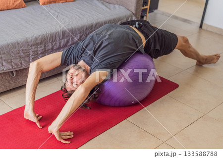 Man practicing yoga at home on a mat, performing calm stretching exercises in a cozy living room, concept of home fitness, mindfulness, balance, health and emotional well-being Man practicing yoga at home on a mat, performing calm stretching exercises in a cozy living room, concept of home fitness, mindfulness, balance, health and emotional well-being 133588788