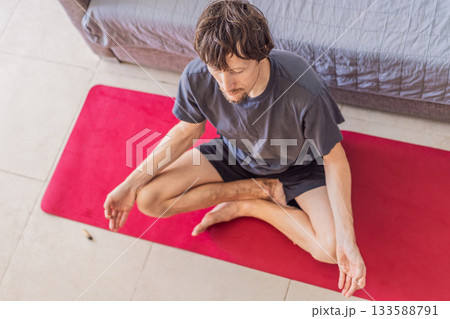 Man practicing yoga at home on a mat, performing calm stretching exercises in a cozy living room, concept of home fitness, mindfulness, balance, health and emotional well-being 133588791