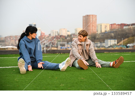 two women friends 50 and 60 years old doing bends forward sitting at a stadium, discussing two women friends 50 and 60 years old doing bends forward sitting at a stadium, discussing 133589457