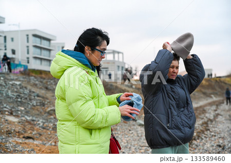 Two Russian women 50 years old and 60 years old walking in cold Vladivostok weather preparing for warmth putting on hats during a calm outdoor moment Two Russian women 50 years old and 60 years old walking in cold Vladivostok weather preparing for warmth putting on hats during a calm outdoor moment 133589460