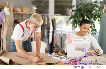 Asian seamstress sews on a machine next to a male fashion designer 133592258