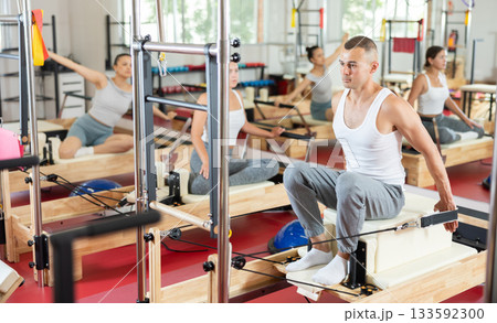 Young guy doing arm exercises on cable reformer device Young guy doing arm exercises on cable reformer device 133592300