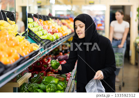 Asian girl in hijab buys ripe bell peppers in supermarket Asian girl in hijab buys ripe bell peppers in supermarket 133592312