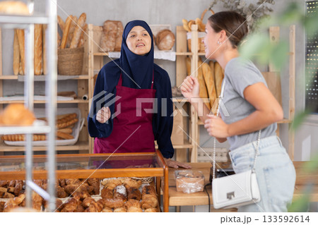 Smiling Arab saleswoman talking to female customer in bakery Smiling Arab saleswoman talking to female customer in bakery 133592614