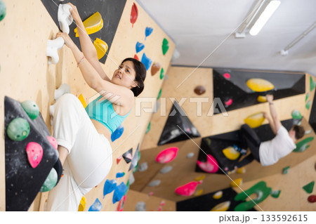 Asian girl is focused on climbing to top of artificial bouldering wall along complicated route track Asian girl is focused on climbing to top of artificial bouldering wall along complicated route track 133592615