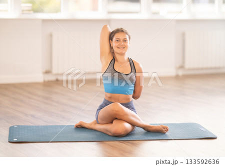 Smiling girl practicing Cow Face Pose in yoga studio Smiling girl practicing Cow Face Pose in yoga studio 133592636