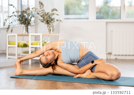 Sportive girl practicing head to knee pose of yoga in light room 133592711