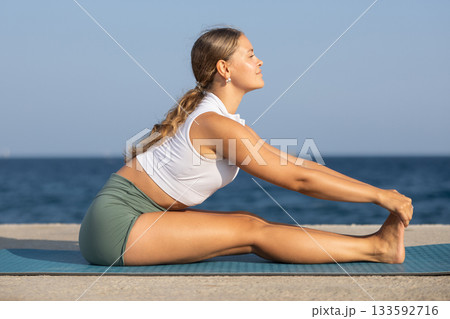 On windy day young slender woman does yoga near sea doing Pashchimottanasana On windy day young slender woman does yoga near sea doing Pashchimottanasana 133592716