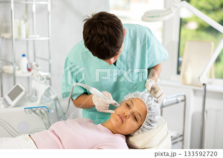 Young male cosmetologist doing cleansing procedure to young woman 133592720