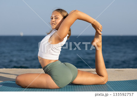 Sportive girl practicing king pigeon pose of yoga on seashore Sportive girl practicing king pigeon pose of yoga on seashore 133592757