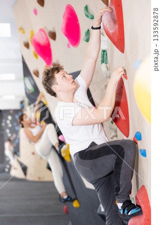 Teen guy practicing rock climbing on climbing wall 133592878