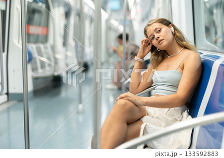 Young woman is sitting in subway car with headphones, getting to work, school. 133592883
