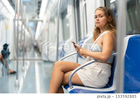 Young woman sitting in subway car with phone 133592885