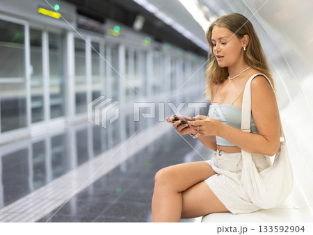 Young girl sitting in subway platform holding phone in hand 133592904