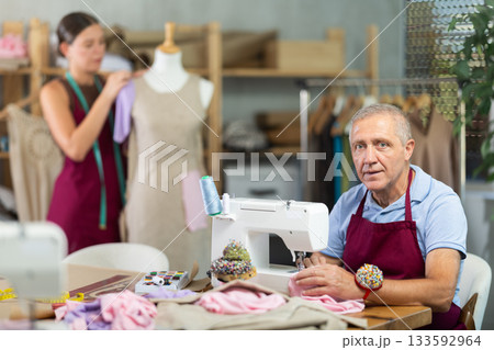 Elderly man sews on machine female assistant sews on mannequin 133592964