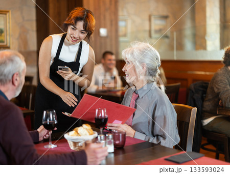 At cafe, Filipino girl waitress communicates with mature couple of customer, accepts order At cafe, Filipino girl waitress communicates with mature couple of customer, accepts order 133593024