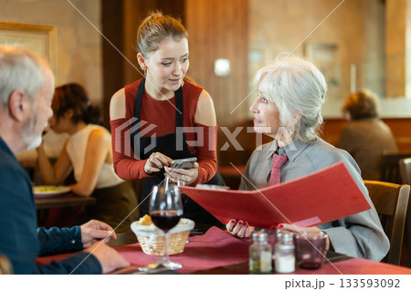 At cafe, girl waitress communicates with mature couple of customer, accepts order 133593092