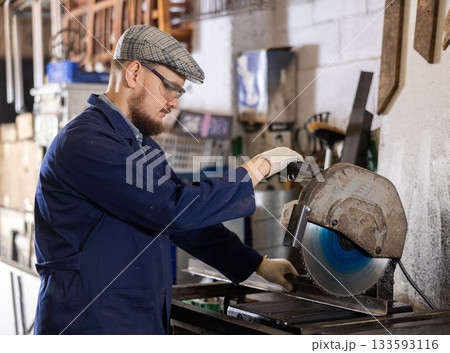 Work in metalworking shop - man wearing safety glasses cuts a metal corner with circular saw Work in metalworking shop - man wearing safety glasses cuts a metal corner with circular saw 133593116