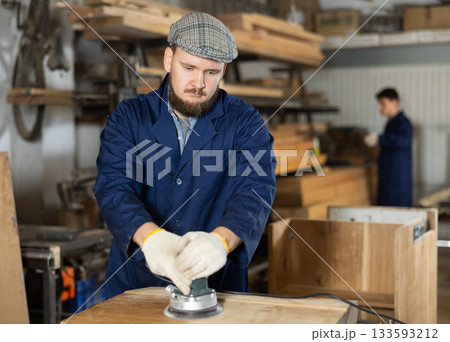 Young man polishing wooden board in workshop Young man polishing wooden board in workshop 133593212