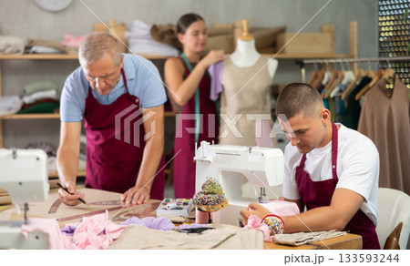 young tailor sews next to a mature worker and a female tailor 133593244