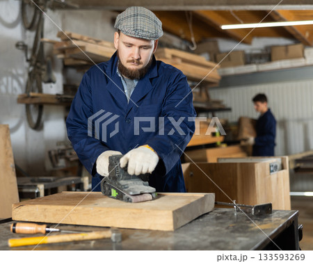 Young man polishing wooden board in workshop Young man polishing wooden board in workshop 133593269