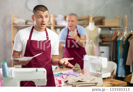 Elderly male tailor scolding assistant with document for dismissal Elderly male tailor scolding assistant with document for dismissal 133593313